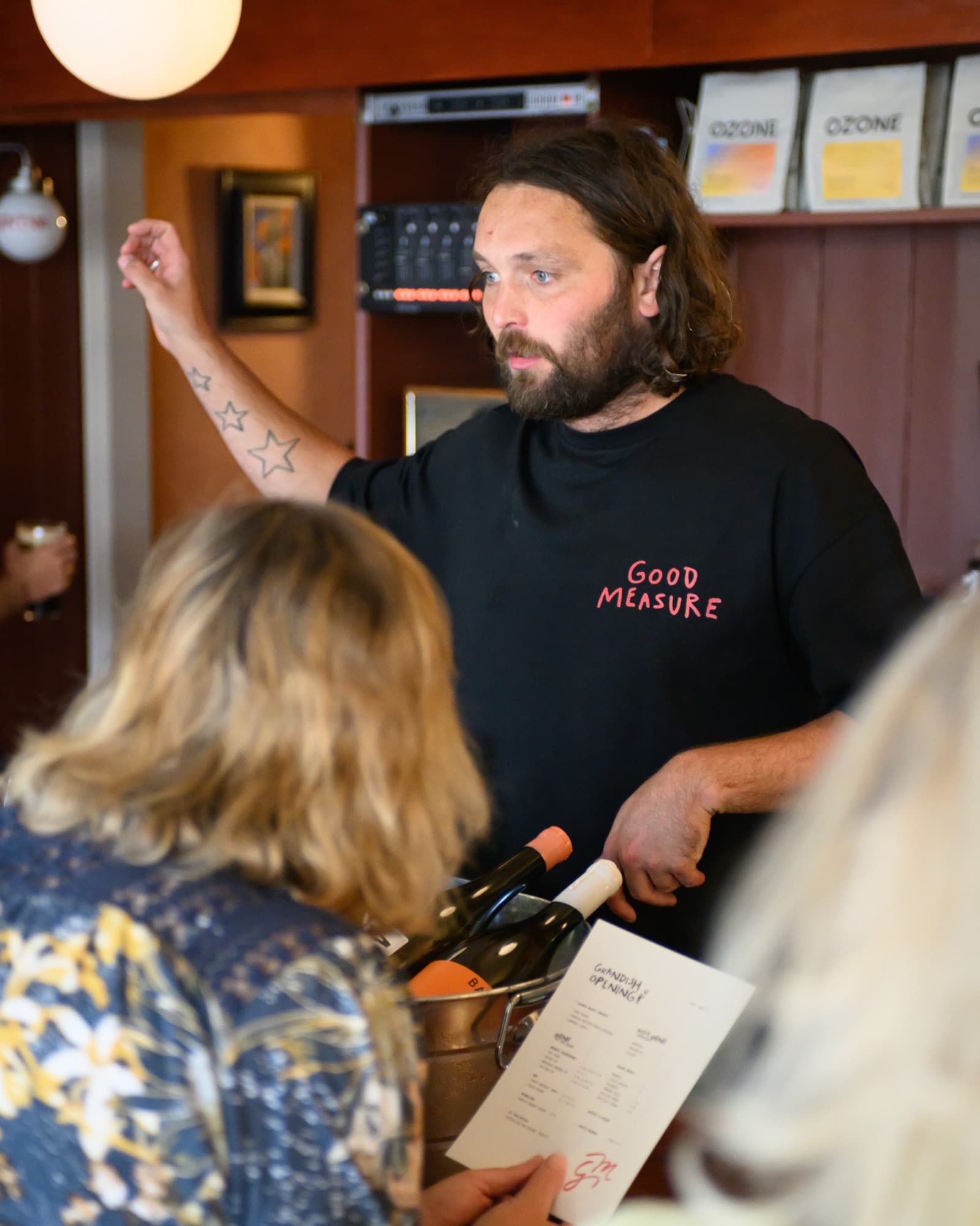 A host in a Good Measure t-shirt talking to a guest across the bar