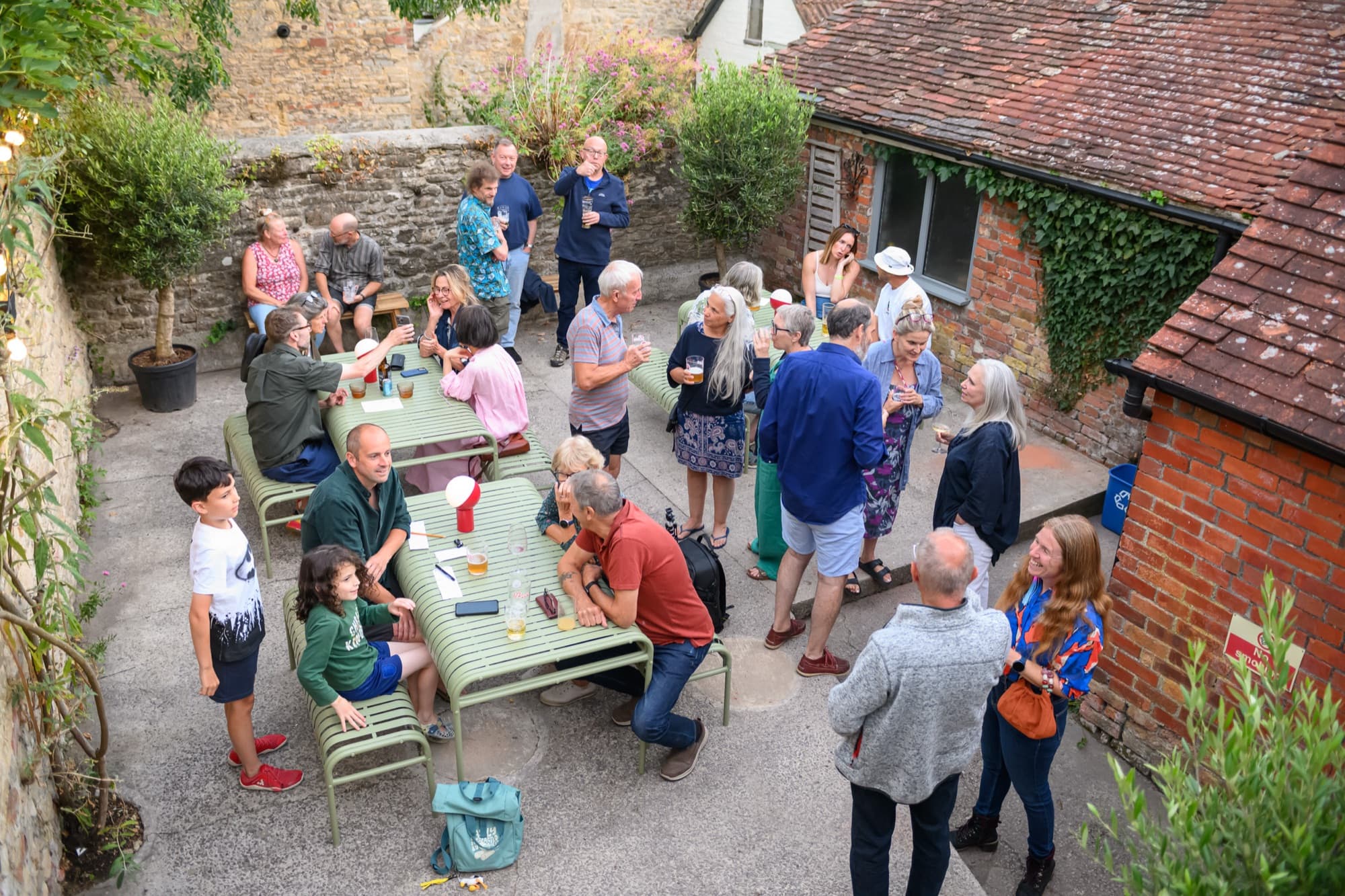 The garden full on a summer evening, people standing and sitting at long tables
