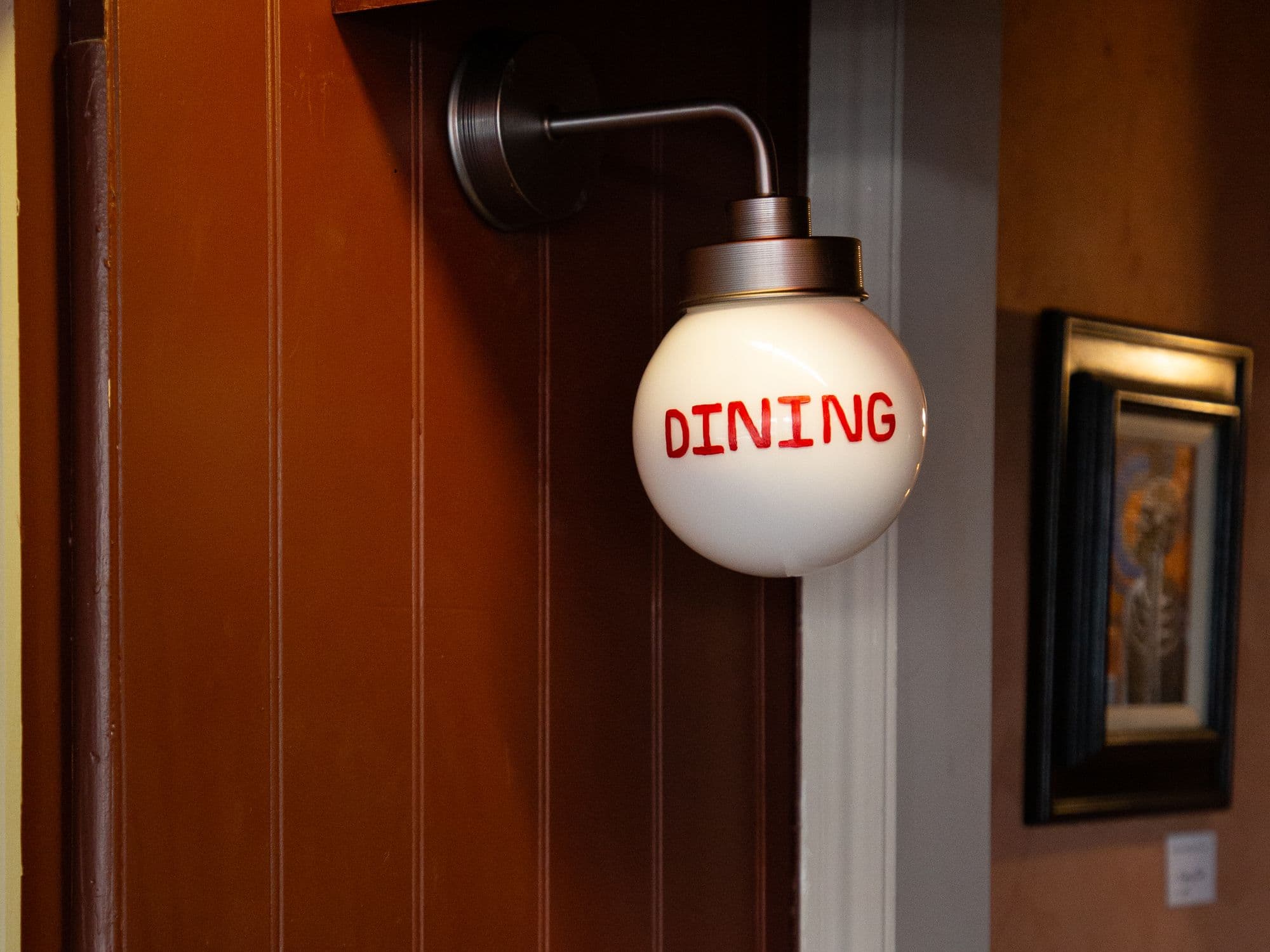 A globe wall light lettered DINING on wooden panelling, a framed painting beside it