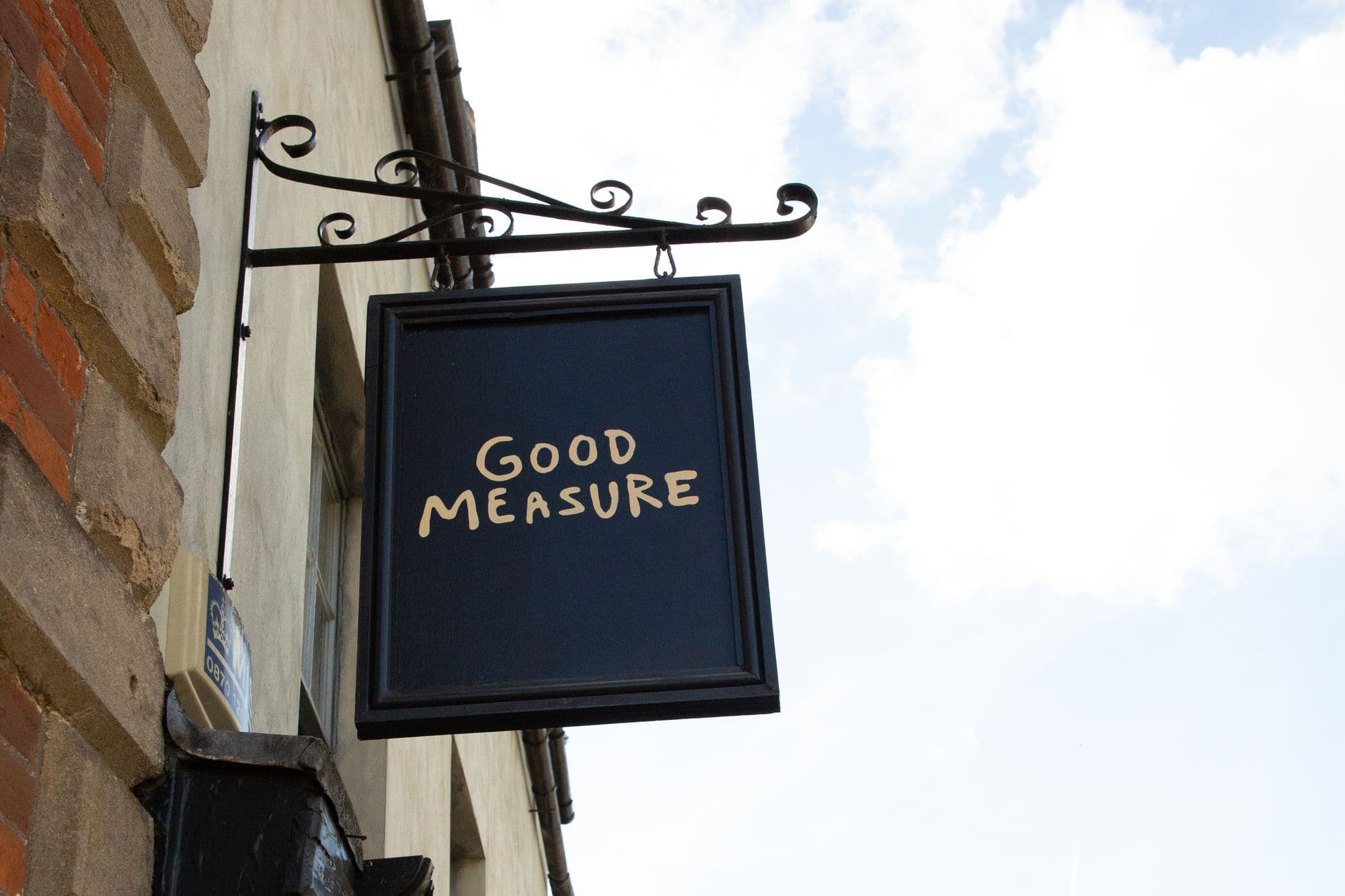 The hanging Good Measure sign on its iron bracket above the shopfront, against a blue sky