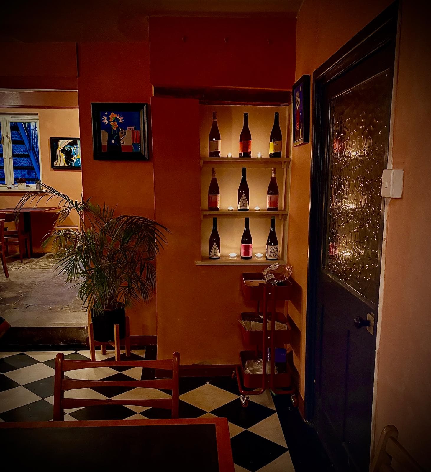 The corner by the front door: nine bottles lit by tealights in a plastered wall niche, with the dining room and its window beyond