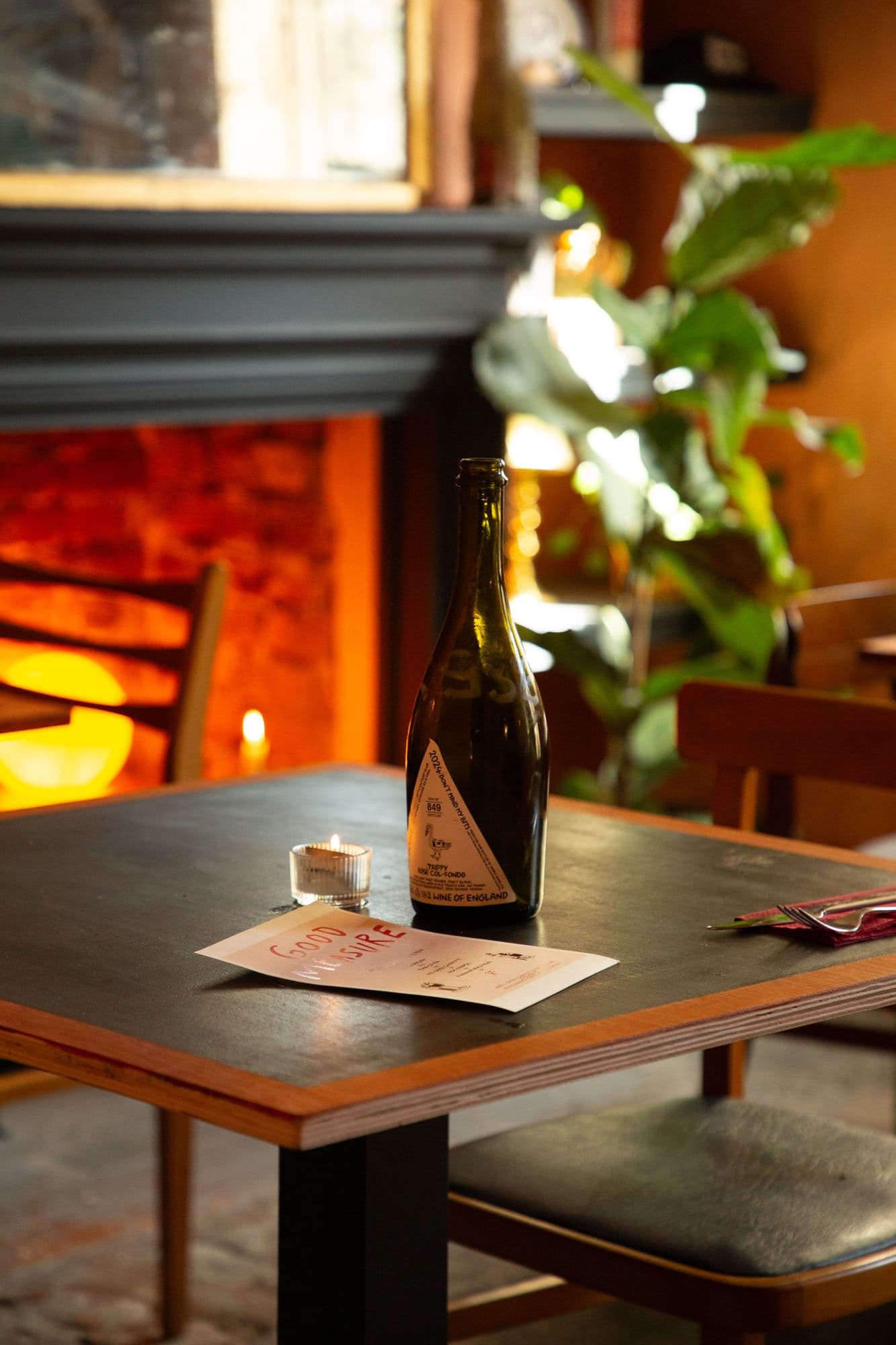 A table in the snug laid with a candle, a bottle of English rosé and a menu card, the fire glowing behind it