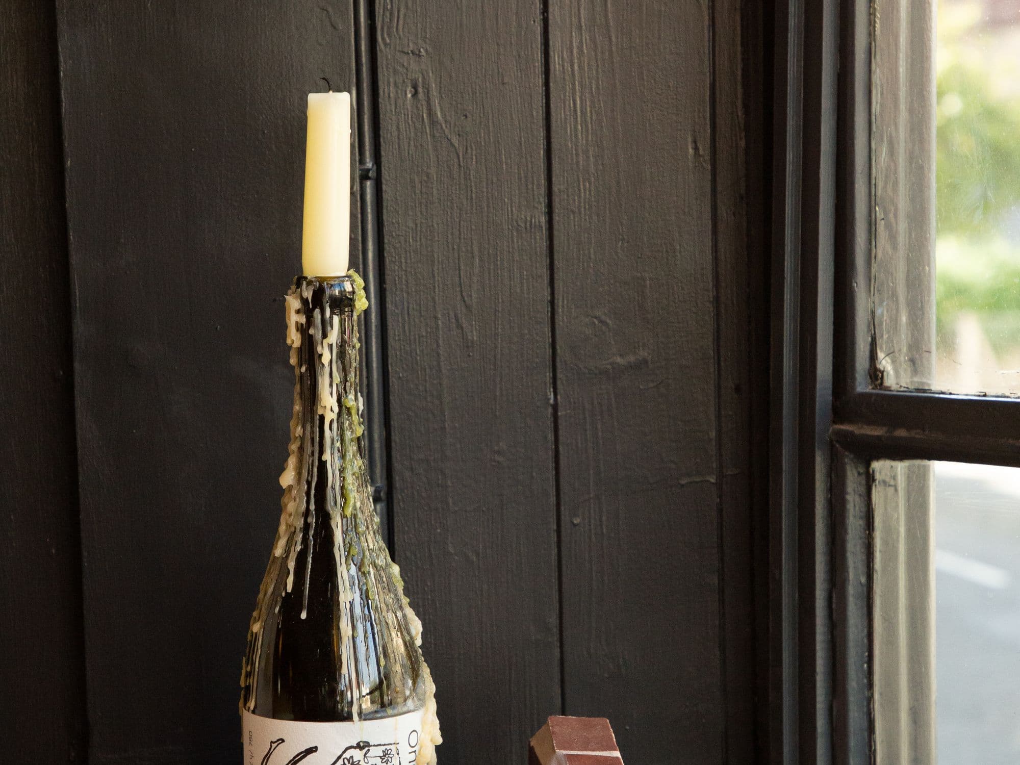 A candle in a wine bottle on the tiled window ledge, against dark painted boards