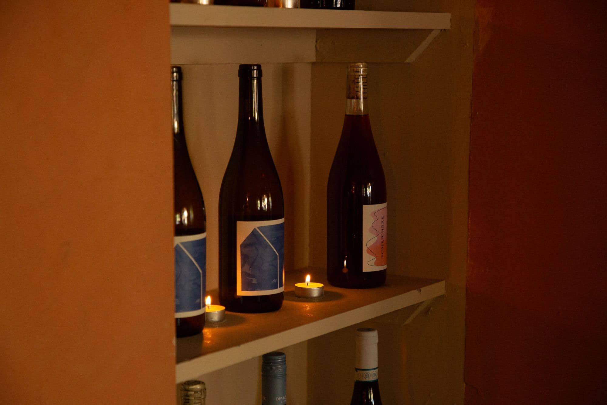 Bottles of wine on a shelf in a plastered alcove, tealights burning in front of them