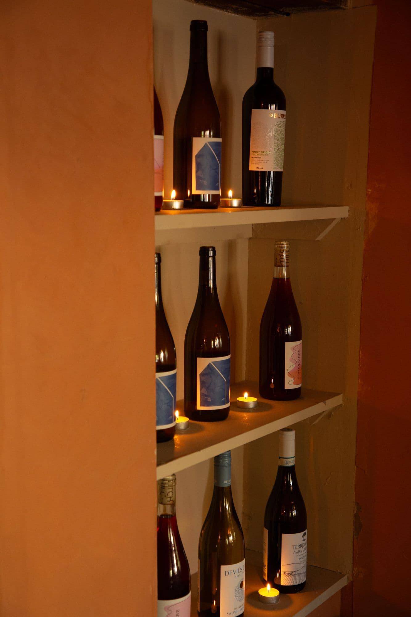 Tall shelves of wine set into a terracotta wall, tealights burning between the bottles
